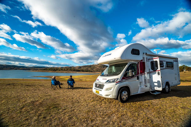 two people sitting outside of an avida motorhome 